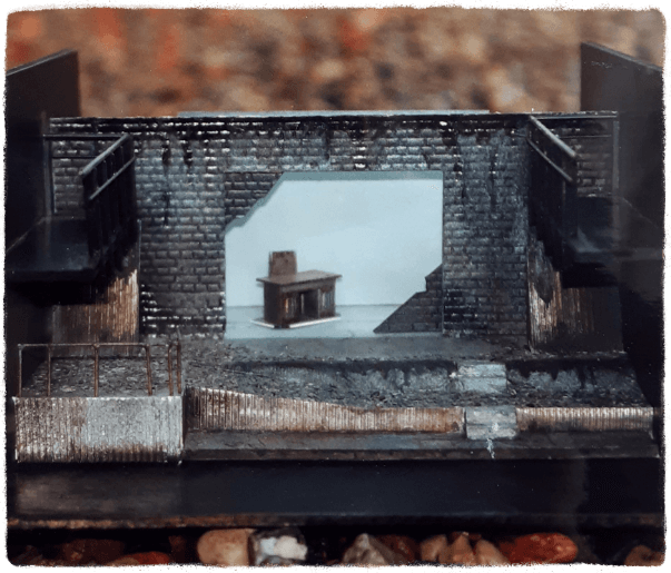 Bühnenmodell "Draußen vor der Tür" Miniatur-Bühnenmodell des Theaterstückes „Draußen vor der Tür“ von W. Borchert mit dunklen Wänden und altem Holzschreibtisch mittig hinter einer Schiebewand.