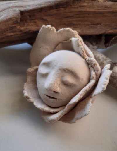 Der helle, kahle, runde Kopf eines kleinen Menschen ist umrandet von Blütenblättern im selben Ton. Die Augen sind geschlossen.