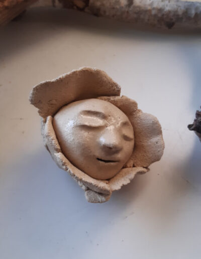 Der helle, kahle, runde Kopf eines kleinen Menschen ist umrandet von Blütenblättern im selben Ton. Die Augen sind geschlossen.