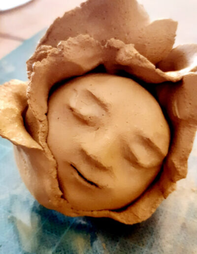 Eine Blütenkind-Plastik in Nahaufnahme und aus hellbraunem Ton liegt auf dem Arbeitsplatz der Künstlerin. Sie ist fertig ausgehärtet und bereit für den ersten Brand.