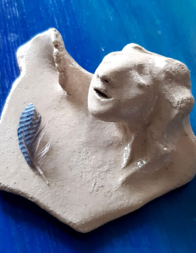 Auf einem kleinen, nicht runden und ohne Vertiefung geformten, Teller ist eine kleine blaue Feder des Eichelhähers abgelegt. Der Teller steht auf blauem Grund. Ein androgyn anmutender Kopf erwächst am Rand. Die Augen sind geschlossen, der Mund geöffnet wie zum Gesang.