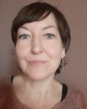 Vera Berg (Handlungsaufruf Malerei) Portrait der Künstlerin Vera Berg vor einer altrosa Wand in einem ähnlich farbigen Wollpullover. Sie lächelt in die Kamera.