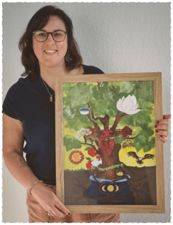 Sandra Schneider steht in dunkelblauem Shirt und hellbrauner Hose mit ihrem Kraftbild in den Händen und lächelt in die Kamera.